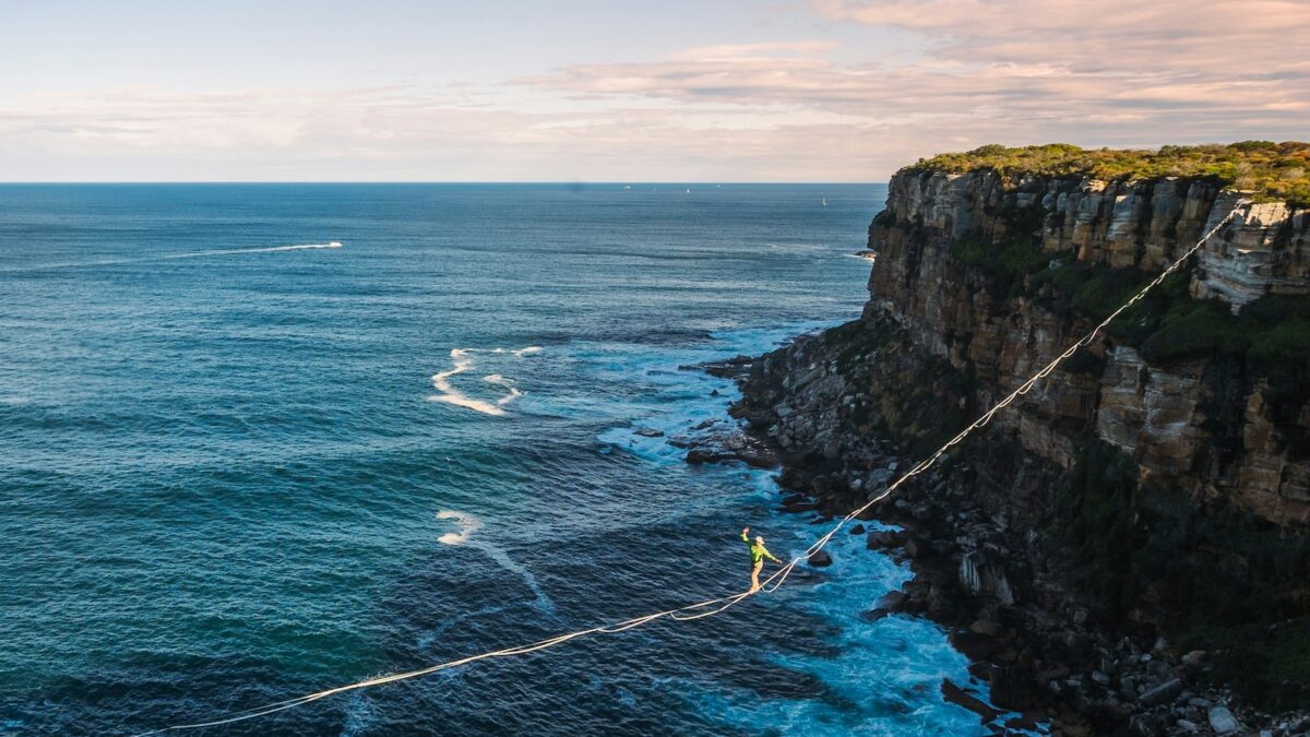 Adapting Your MVP in Real-Time. Tightrope walker balancing over the ocean between cliffs, symbolizing risk and strategy.