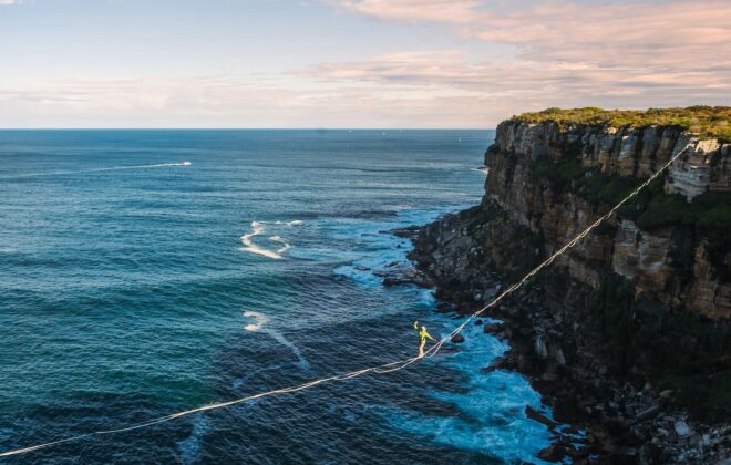 Adapting Your MVP in Real-Time. Tightrope walker balancing over the ocean between cliffs, symbolizing risk and strategy.