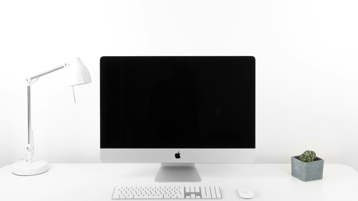 Streamlining MVP Development with AI. Minimalist workspace with an iMac, white desk lamp, and potted plant, symbolizing a clean and efficient work environment.